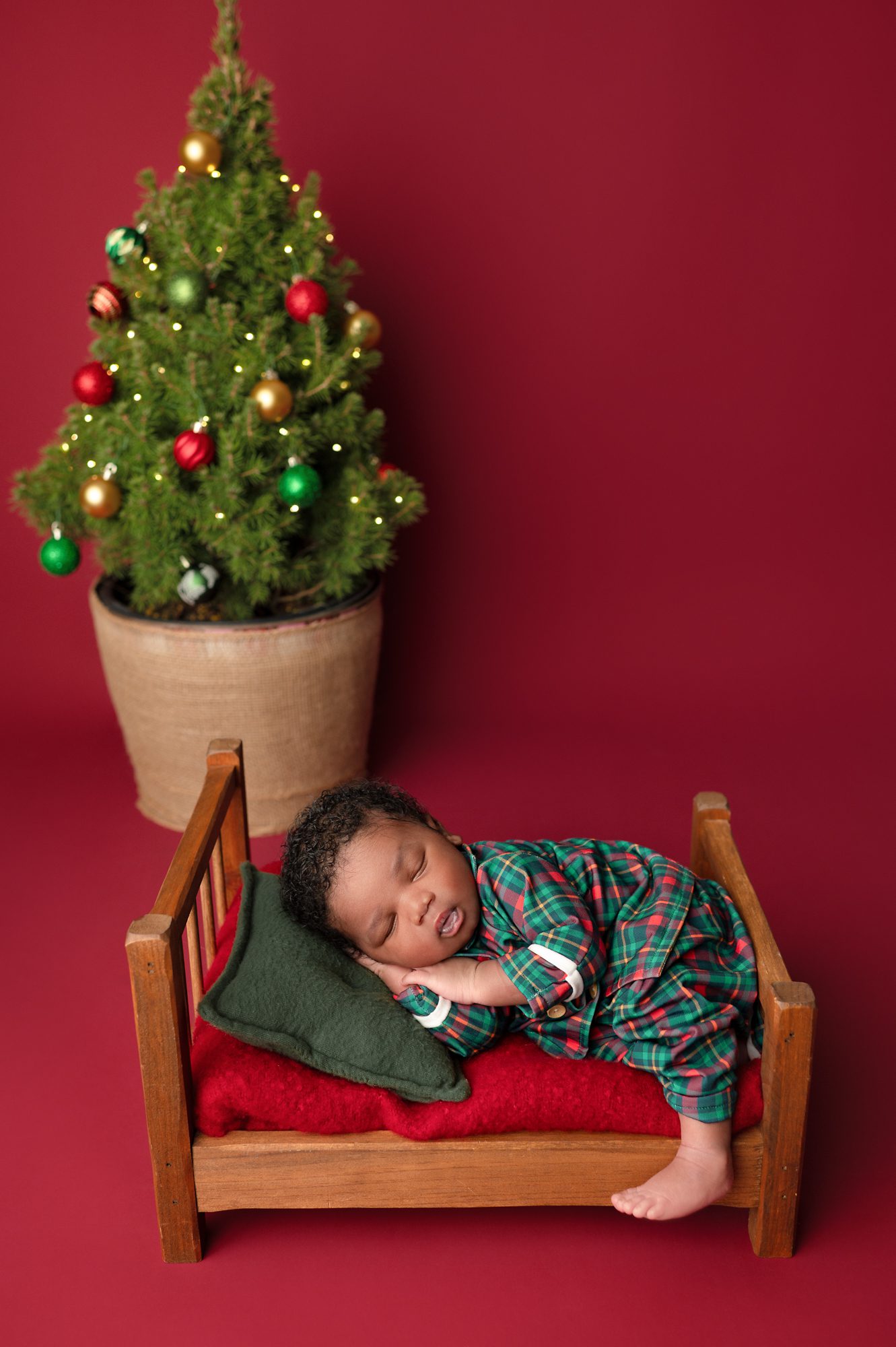 newborn baby lying in bed in Christmas pajamas in front of a Christmas tree