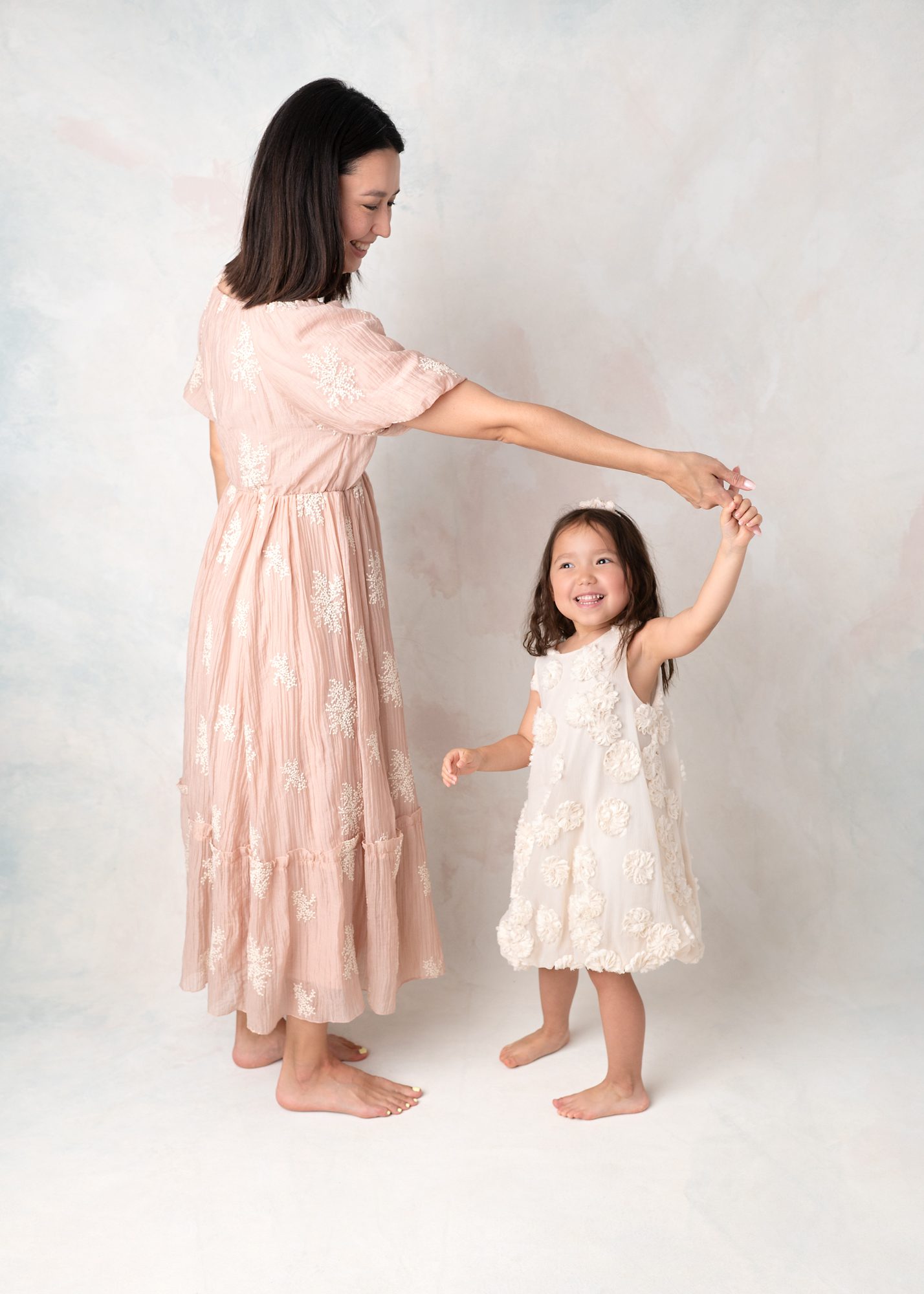 Mommy and me portrait on fine art canvas background. Mom is twirling smiling daughter